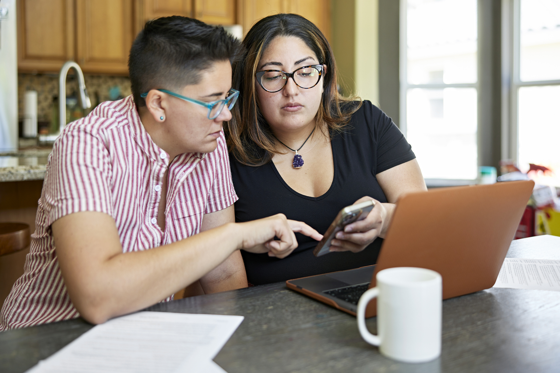 Two people looking at phone and laptop